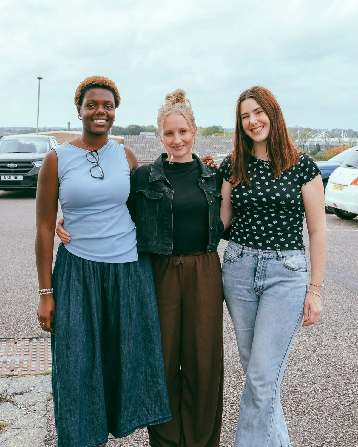 Three young women from Covenant Life Church smiling arm in arm outside on a Sunday