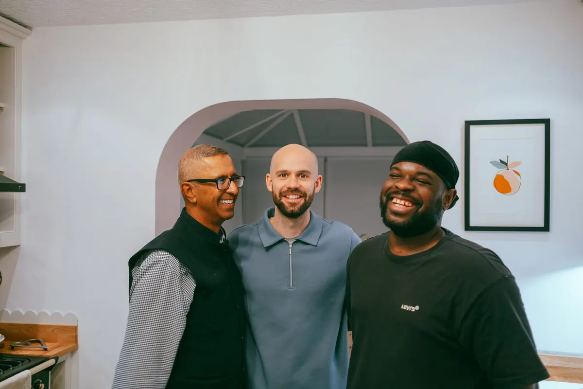 Three men smiling side by side at a Life Group in a home kitchen