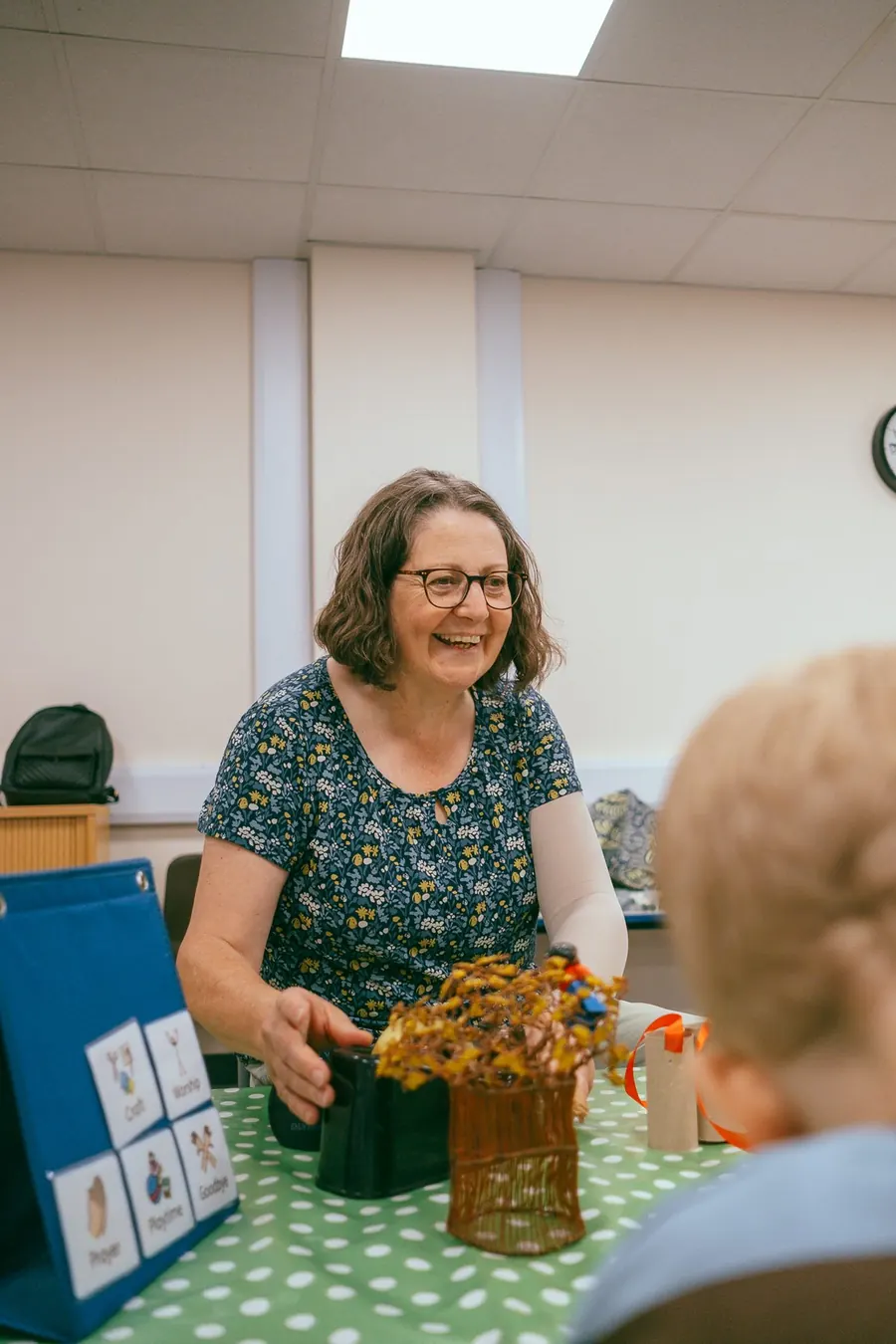 A smiling woman at a table with a polka dot cloth and a basket of dried flowers