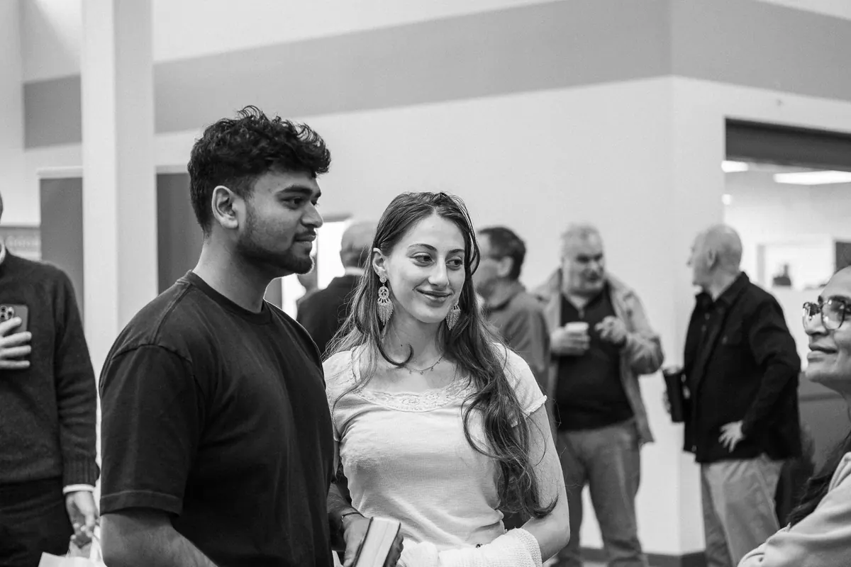 Black and white photo of a young man and woman talking in a busy church hall