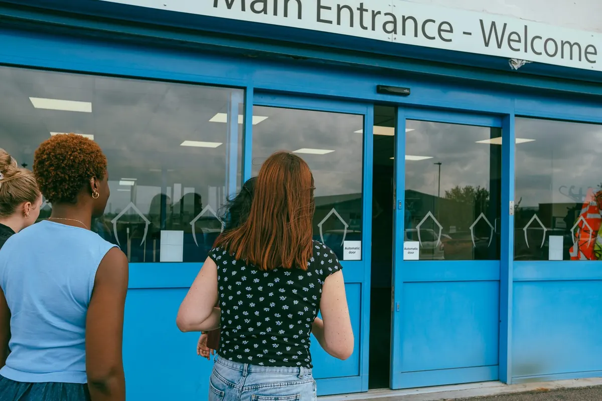 Two women walking up to the blue doors under a sign reading Main Entrance, Welcome